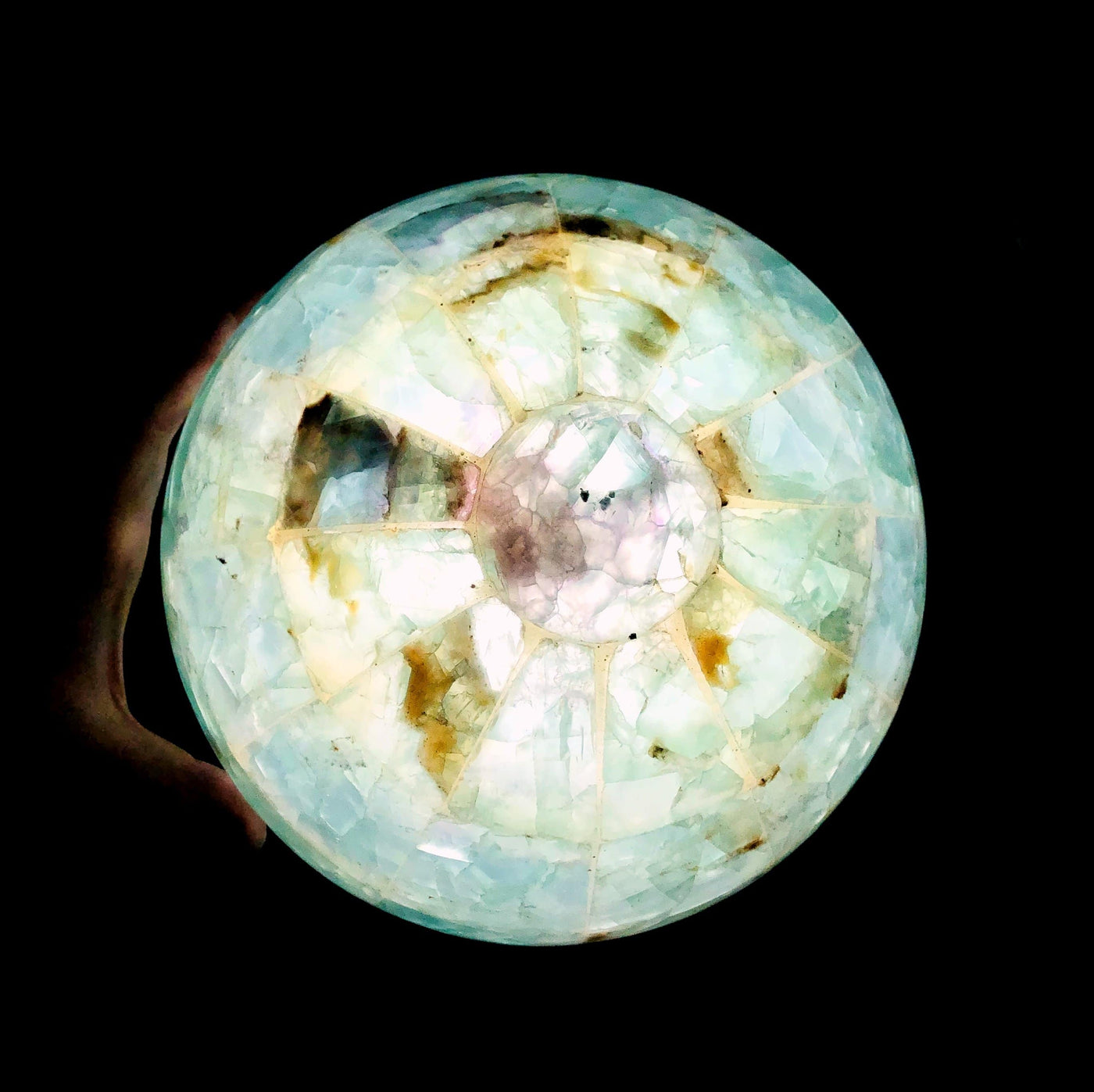 Rainbow Fluorite Sphere Lamp lit up in dark room with hand touching it