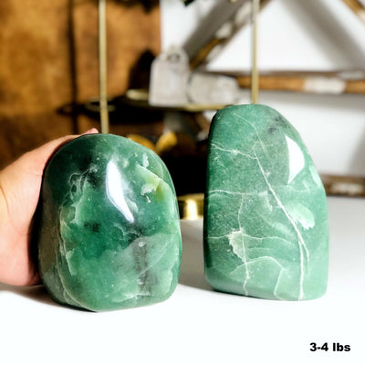 hand holding 3-4lbs aventurine cut base with another next to it with decorations blurred in the background