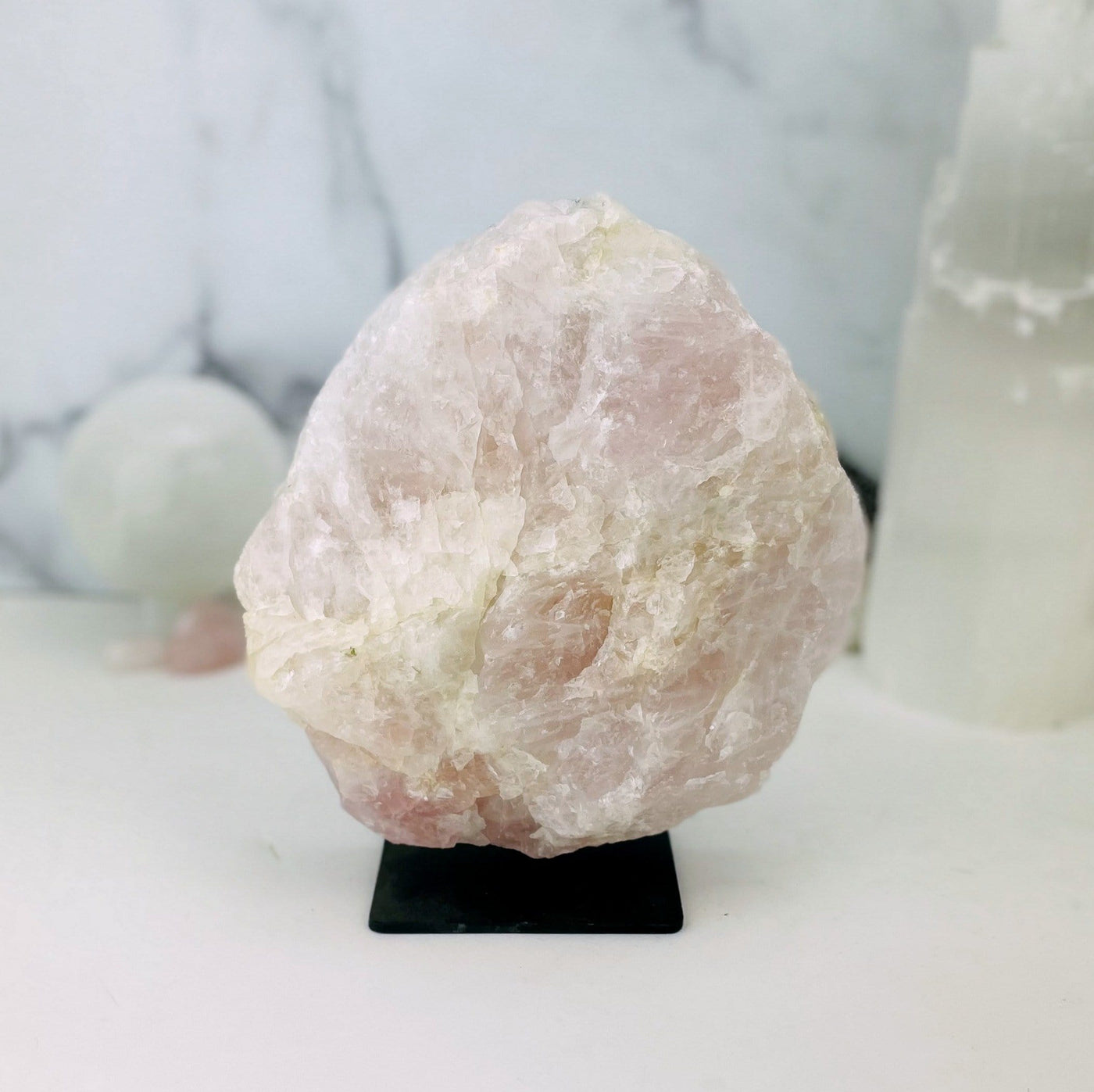 Rose Quartz on Metal Stand with other crystals blurred on marble background