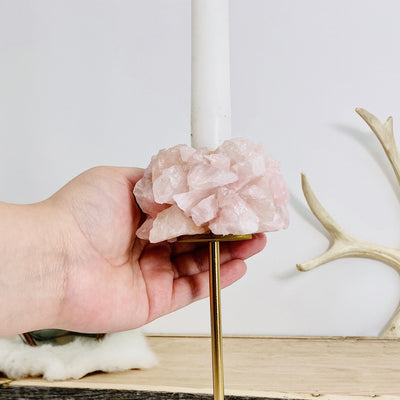 Hand holding Rose Quartz Taper Candle Holder with decoration in the background