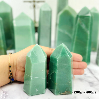 Two 200-400g towers next to a woman's hand with larger green quartz towers in the background.