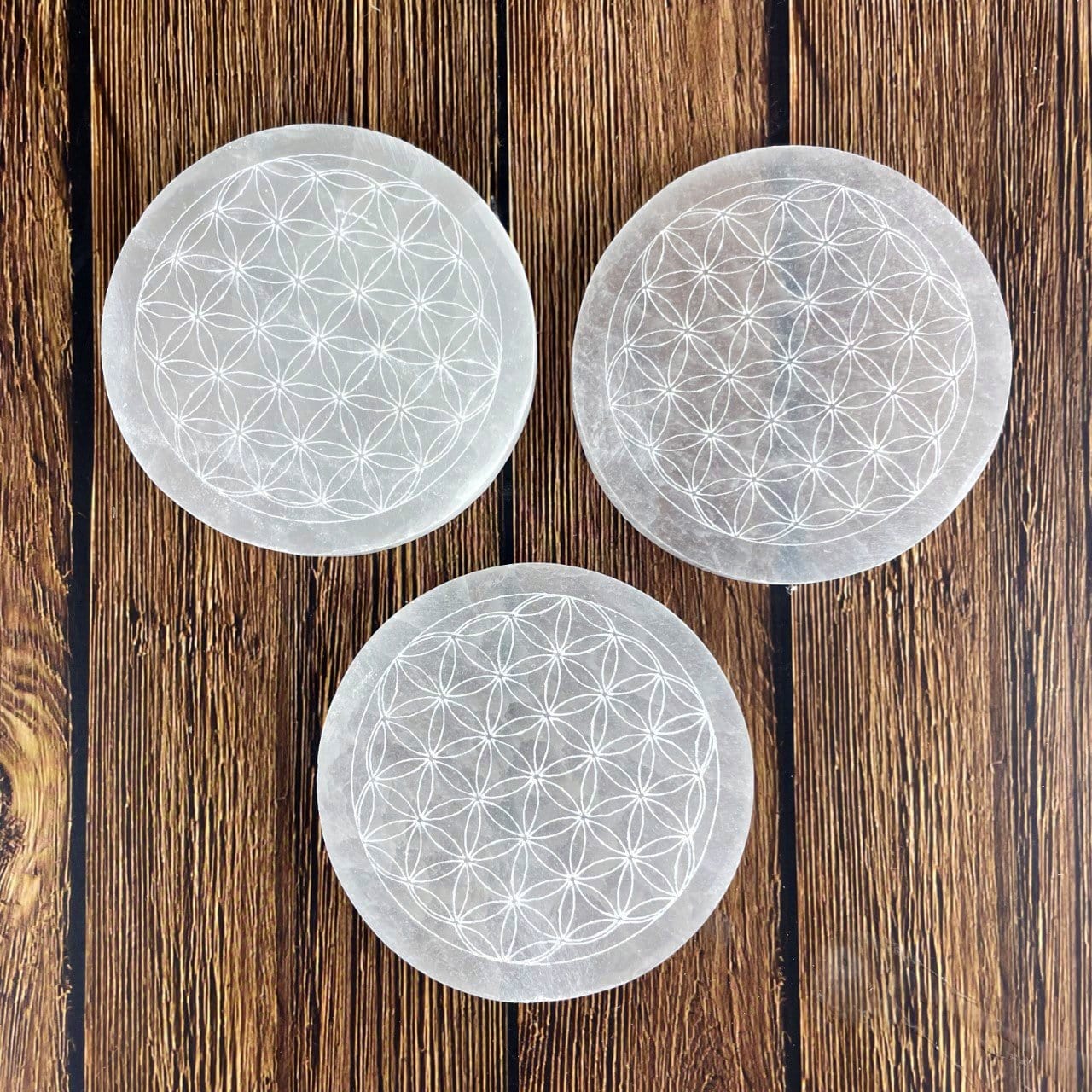 overhead closeup of three selenite round plates engraved with flower of life for engraving details and possible variations
