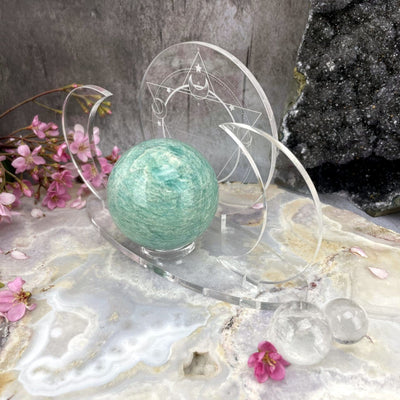 Shown from an angle - Acrylic Sphere Holder Crescent Moons - Six Pointed Star holding a sphere in an alter surrounded with flowers and crystals.