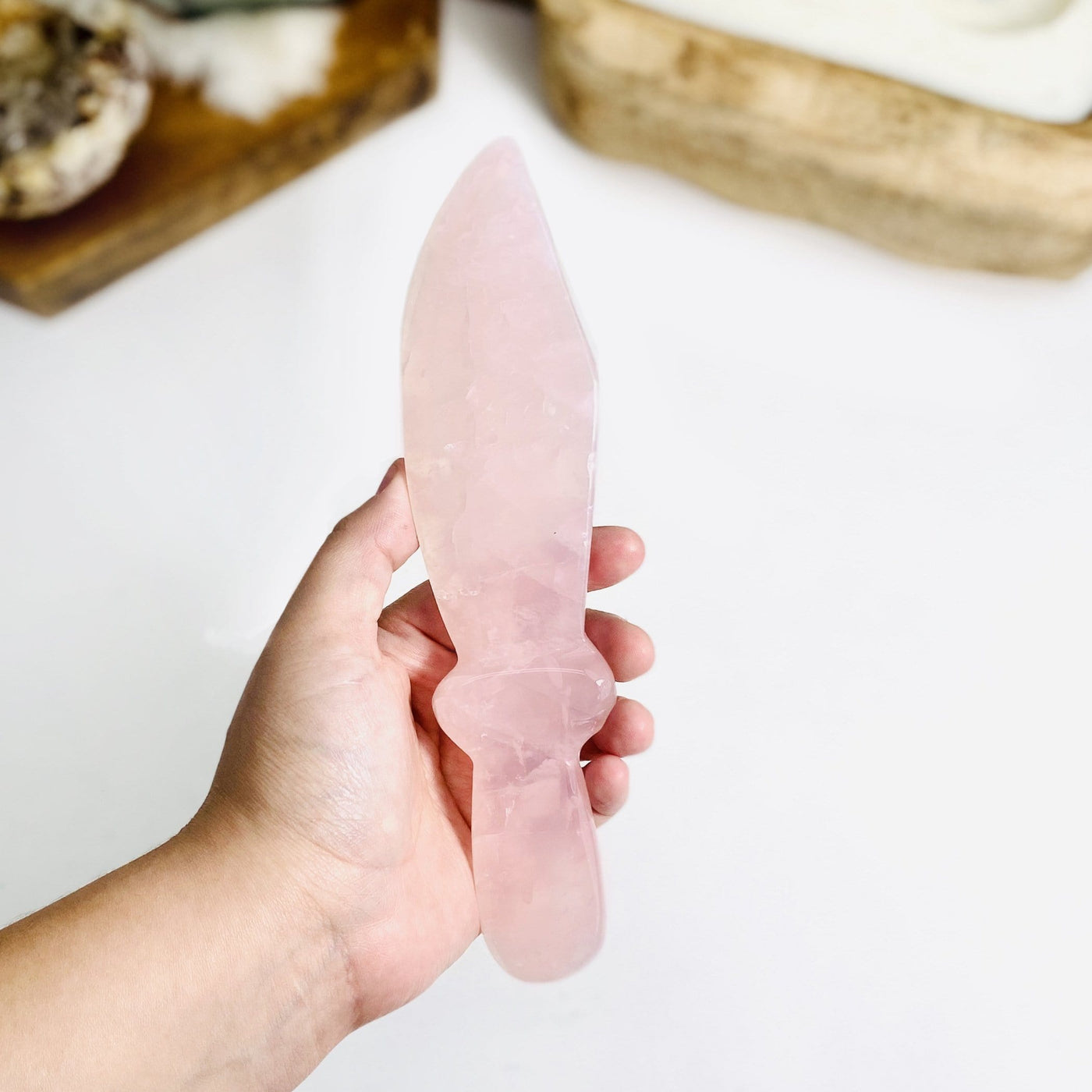 Hand holding up Rose Quartz Knife with decorations blurred in the background