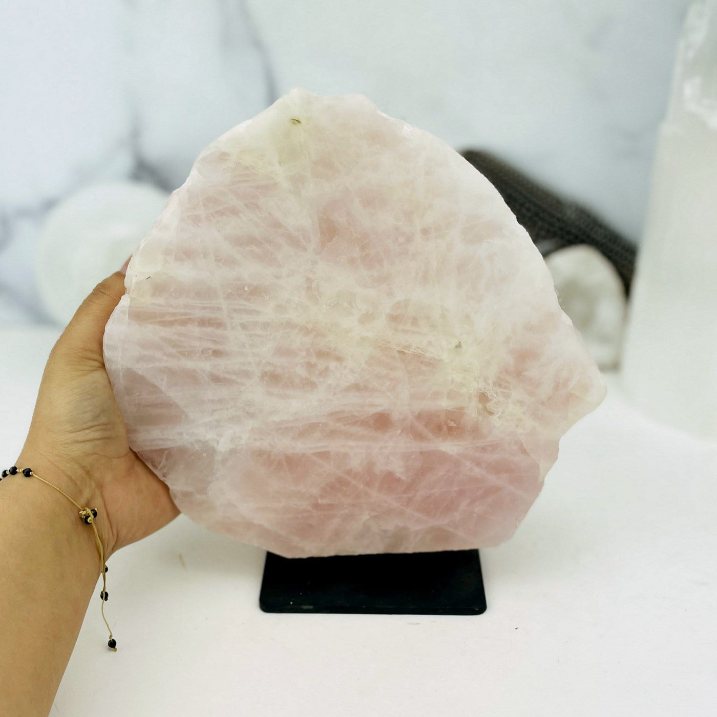 Hand holding onto Rose Quartz on Metal Stand with marble background
