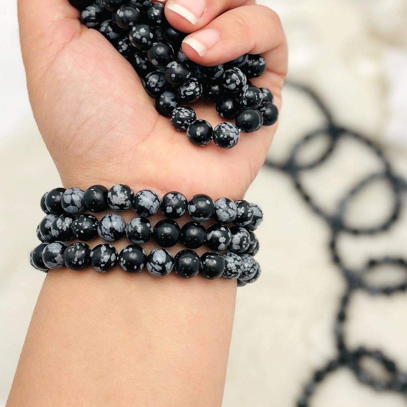 close up of three snowflake jasper round bead bracelets on wrist with many others in hand and in background for size reference and possible variations