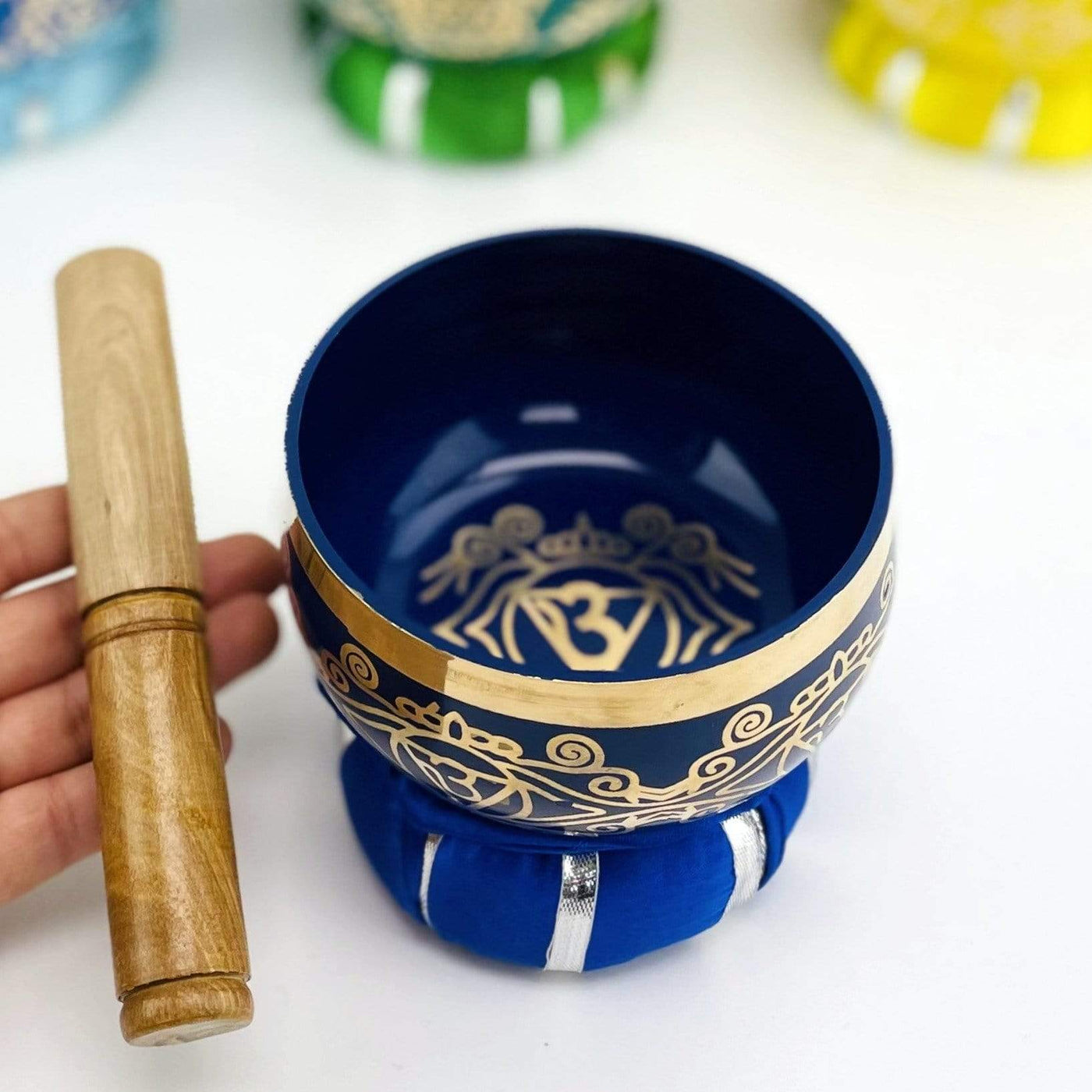 Brass Tibetan Chakra Singing Bowl on top of a pillow and a hand holding the mallot