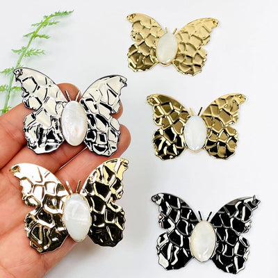 gold and gunmetal butterfly pendants with a mother of pearl center in hand for size reference 