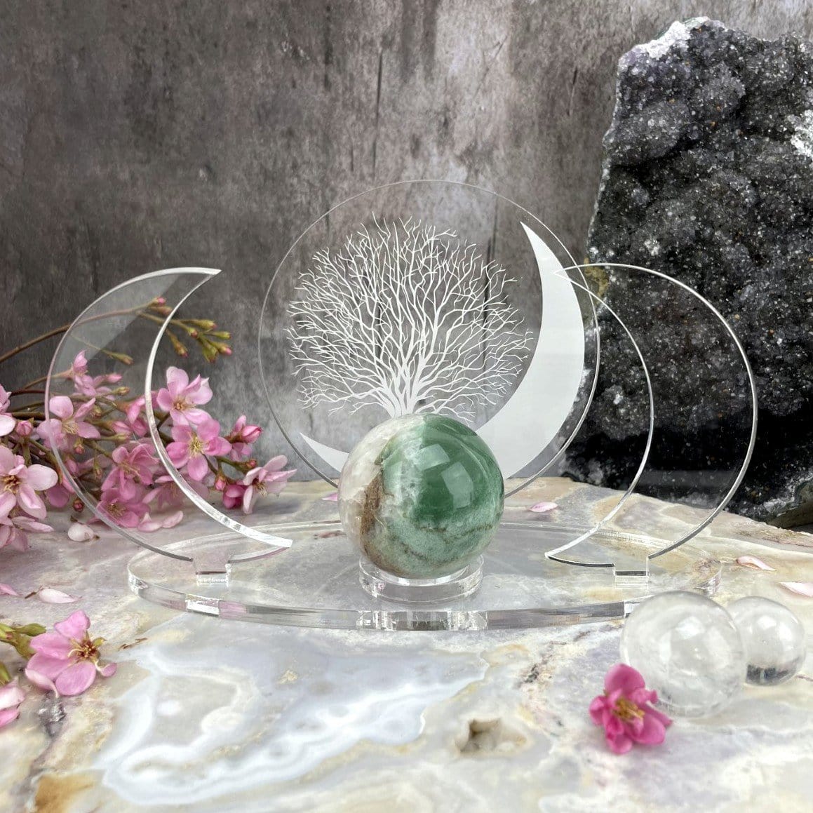 Close up of a front facing Acrylic Sphere Holder Crescent Moons - Tree of Life holding a sphere in an alter that consists of flowers and crystals.