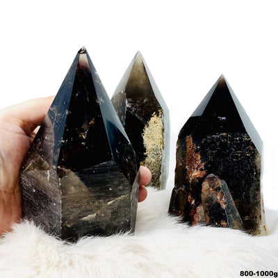 three 800g - 1kg smokey quartz semi polished points on display for possible variations with one in hand for size reference