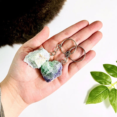 Hand holding up 2 Rainbow Fluorite Silver Toned Key-Chains with various decorations on white background