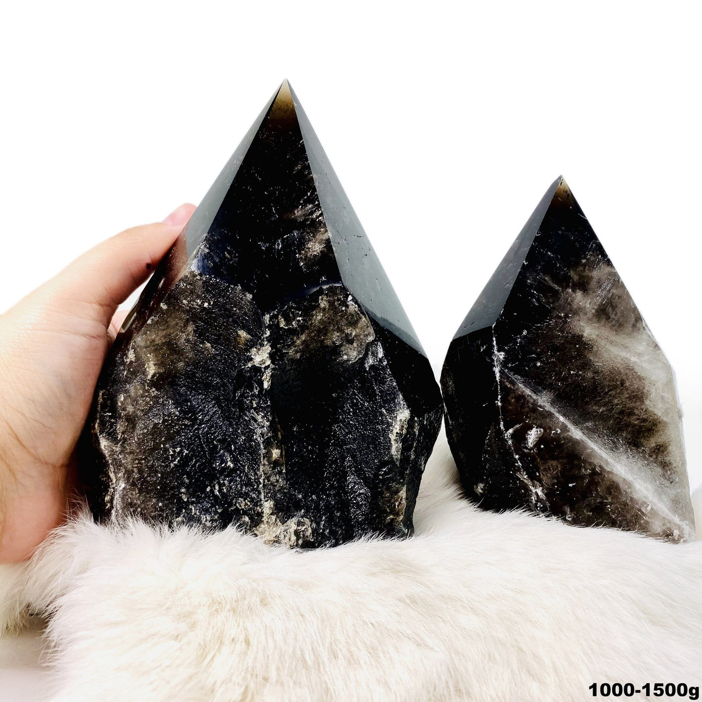 two 1000g - 1500g smokey quartz semi polished points on display for possible variations with one in hand for size reference