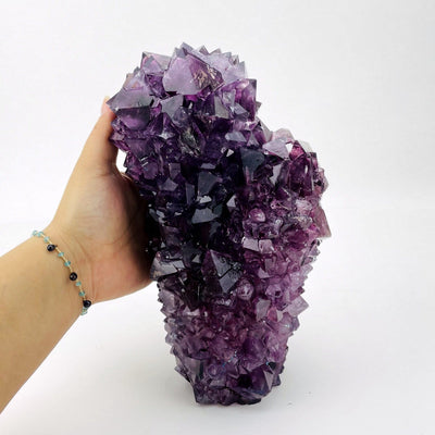 large purple salt crystal formation in hand for size reference