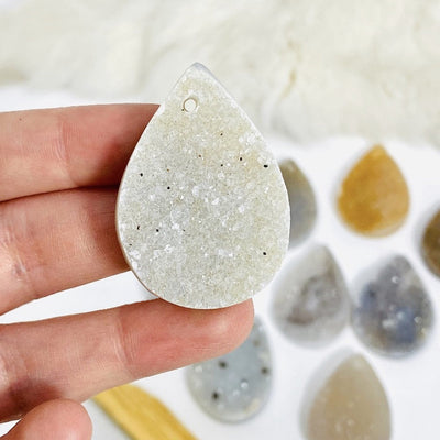 A Hand holding a white teardrop cabochon , top drilled piece 