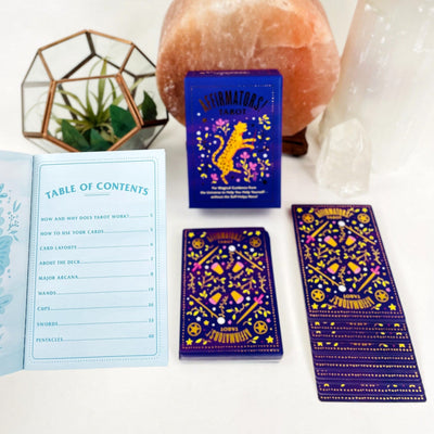An open Affirmation Guidebook displaying Table of Contents with a card deck box in the background with an expanded card deck.