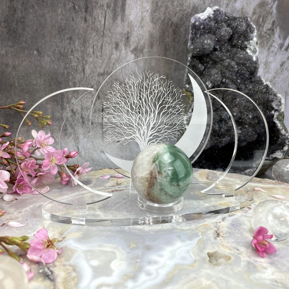 Close up of an Acrylic Sphere Holder Crescent Moons - Tree of Life holding a sphere in an alter that consists of flowers and crystals.