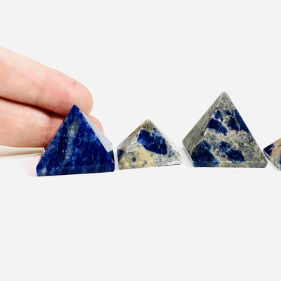 three sodalite pyramids on white background with two fingers behind one for size reference