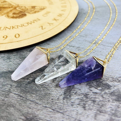 Rose Quartz Amethyst and Crystal Quartz Pendulum Necklaces in gold finish on a table close up