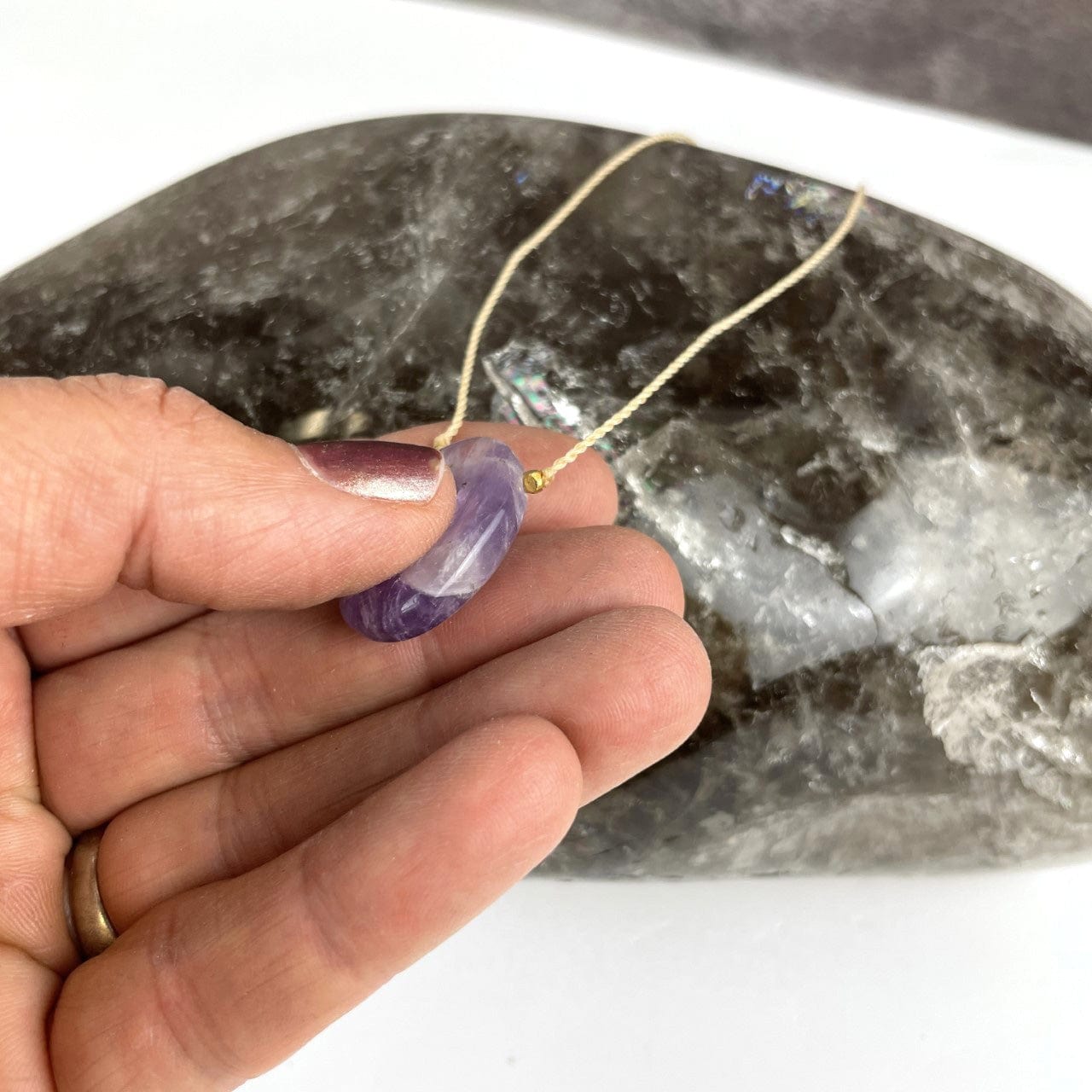 amethyst worry stone necklace in a hand held  with thumb in indention