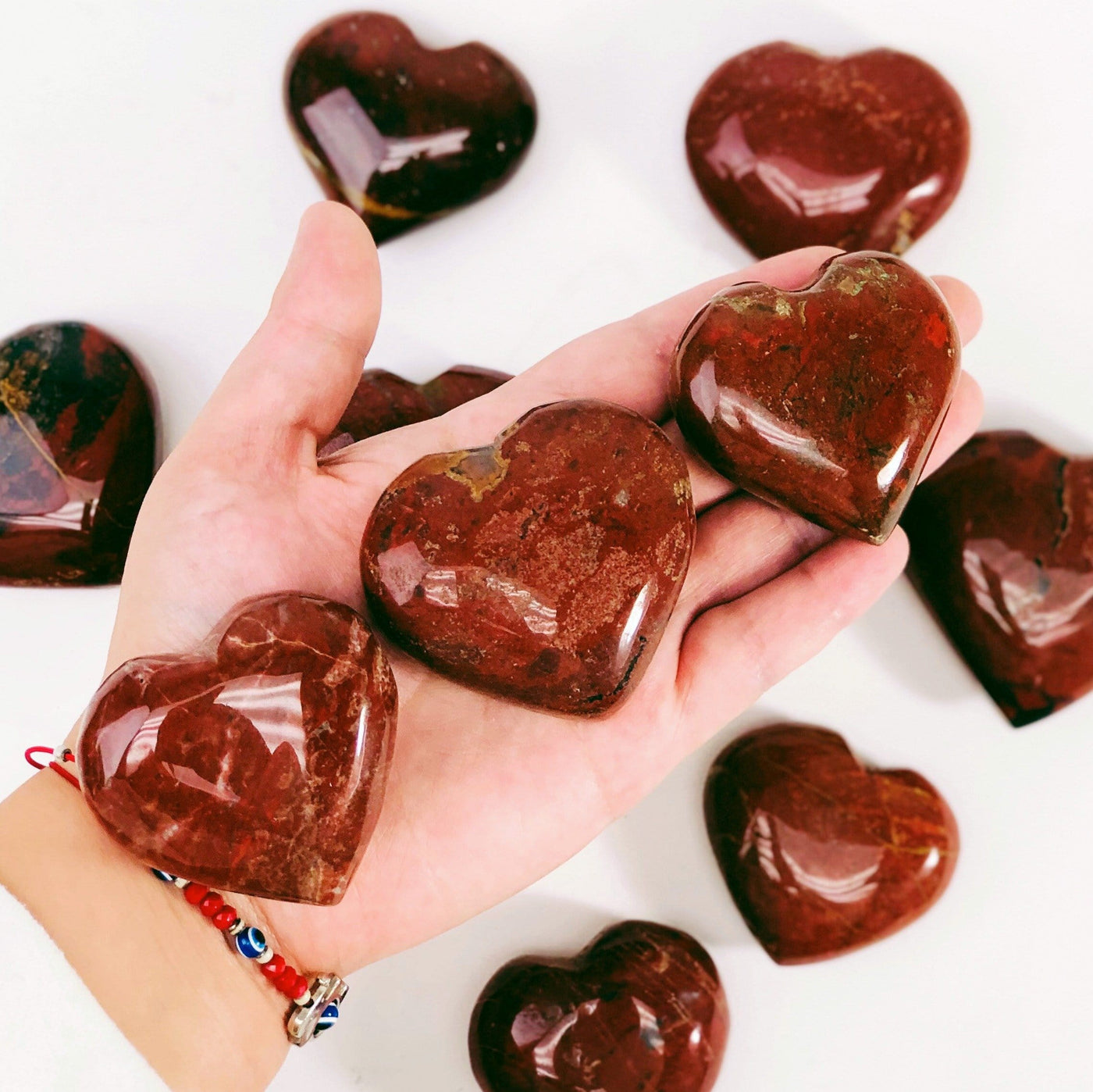 Hand holding up 3 Red Jasper Heart Shaped Stones with others blurred in white background