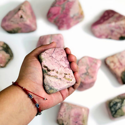 Hand holding up Rhodonite Tumbled Polished Stone with others blurred in the background
