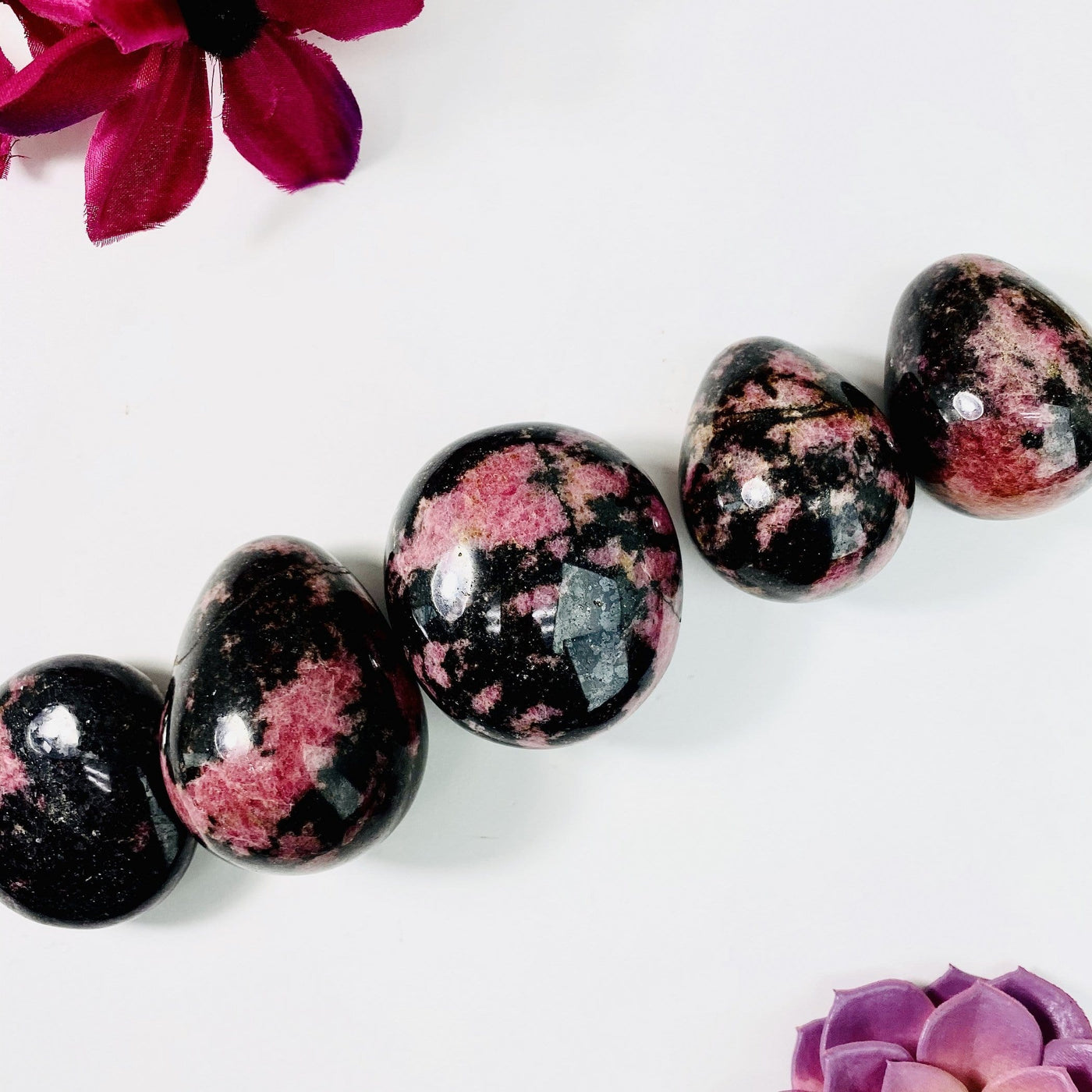 Rhodonite Palm Stones in a line on a white background with flowers