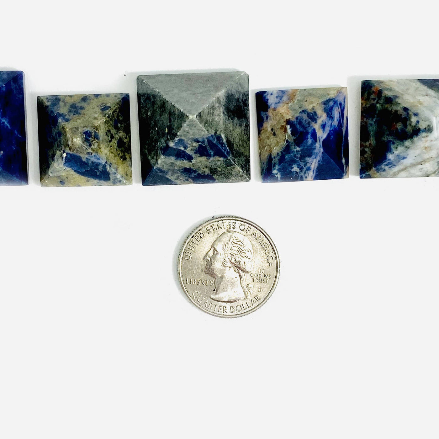 overhead view of four sodalite pyramids on white background with quarter for size reference