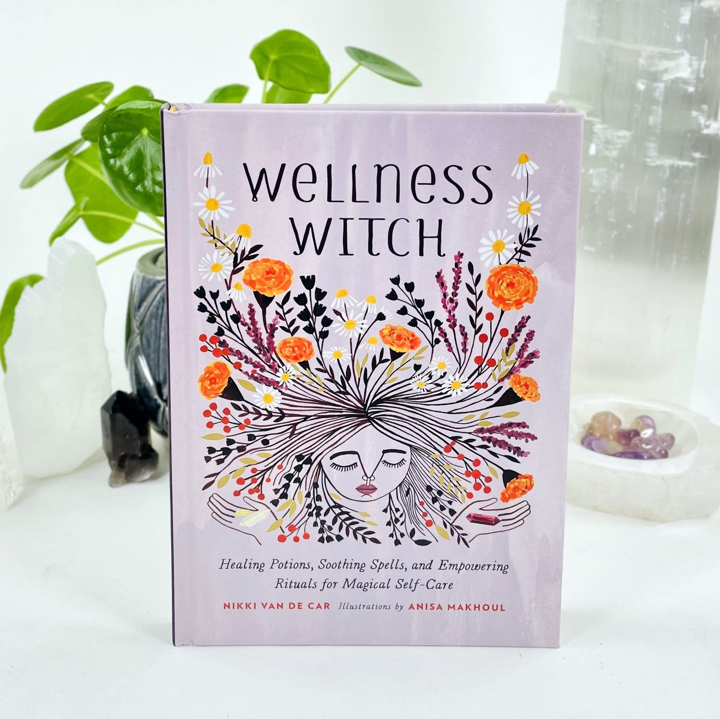 Front cover of the book Wellness Witch.  It is light purple with a woman's face surrounded by flowers.