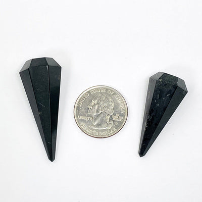2 tourmaline points next to a quarter for size reference on white background