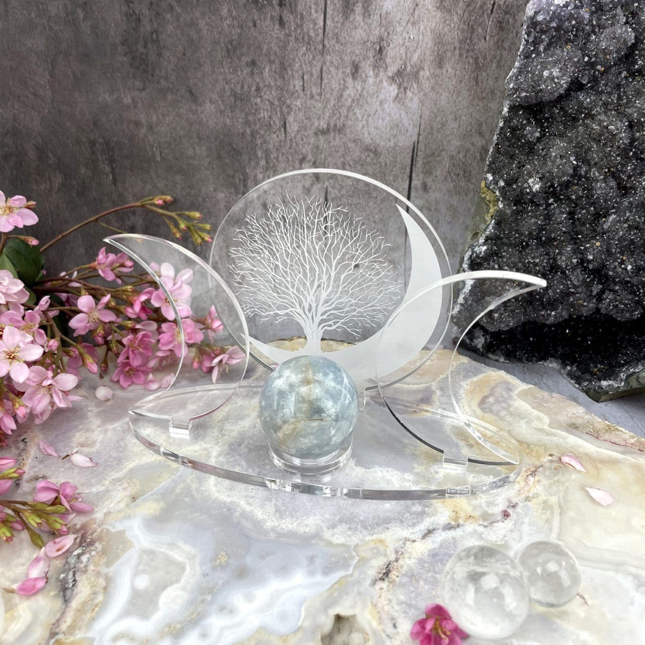 An Acrylic Sphere Holder Crescent Moons - Tree of Life holding a sphere in an alter that consists of flowers and crystals.