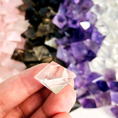 Gemstone Octahedron in clear quartz in a hand showing it is fingertip size, with others in the background 