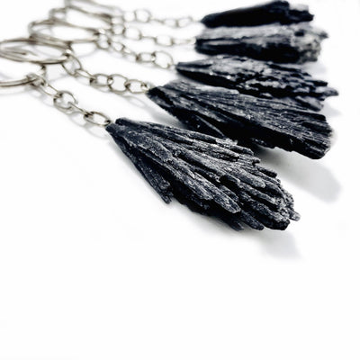 Side view of 5 black kyanite keychains on a white background.
