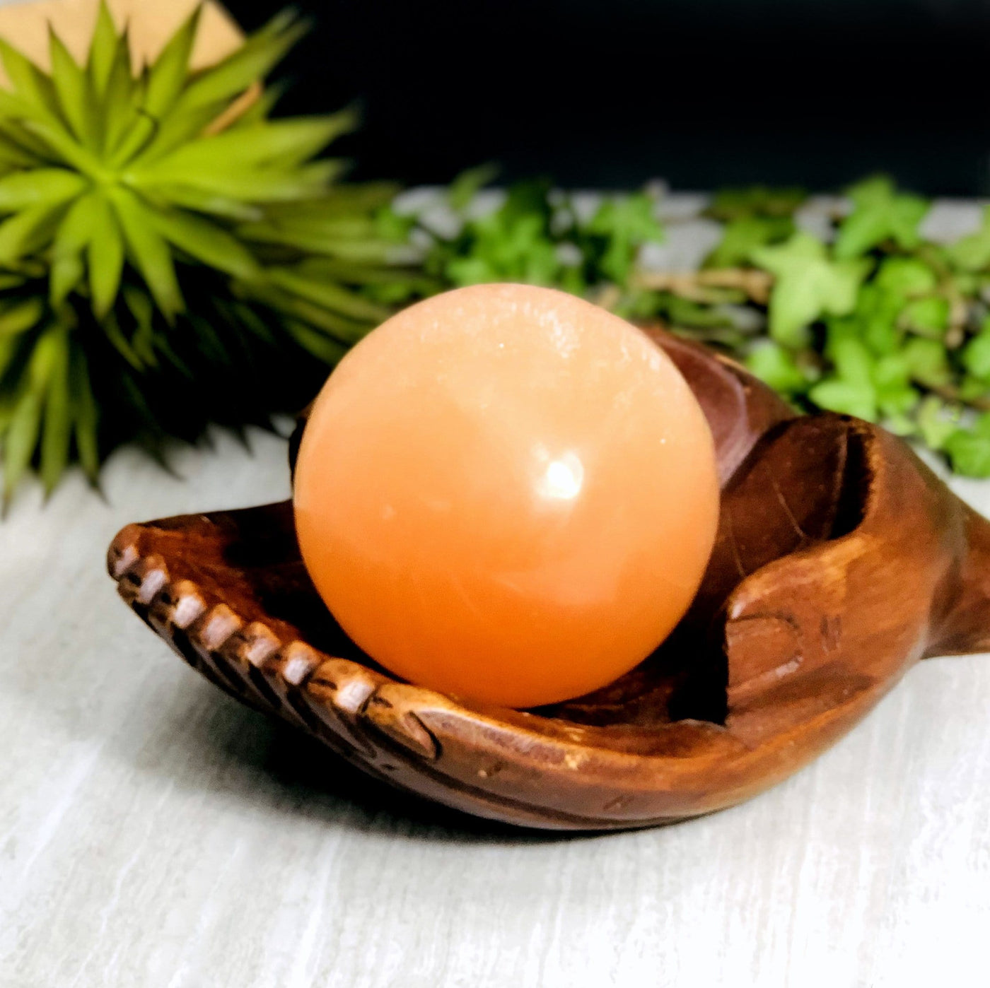 wooden hand bowl holding Orange Selenite Sphere with decorations in the background