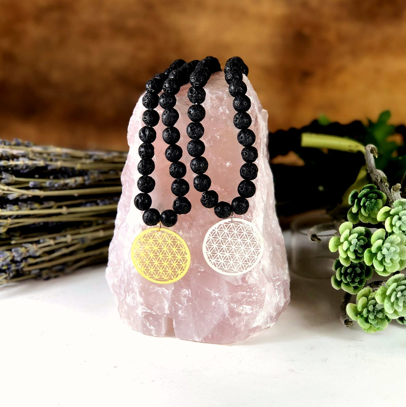 Diffuser Necklace Lava Bead with Flower of Life Charm in Gold/Silver tone in Top Of Rough Rose Lamp on Brown Background.