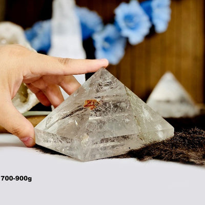hand holding 700-900g Crystal Quartz Pyramid with decorations in the background