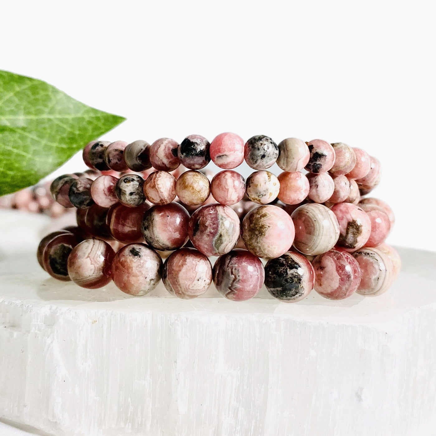 4 Rhodochrosite Round Bead Bracelets stacked on top of each other on selenite slab