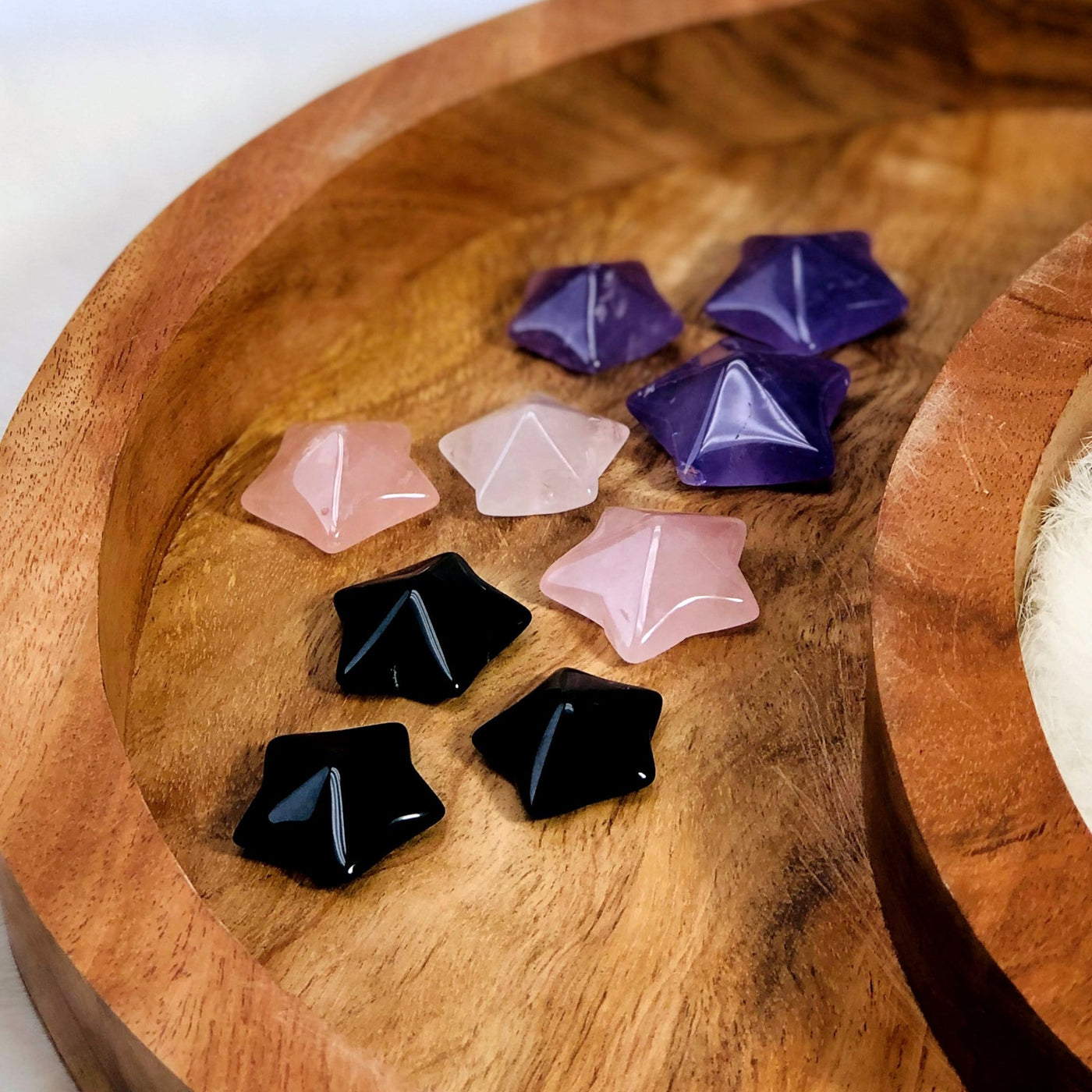 Up close angled view of Nine Puffy Star Cabochon Gemstones displayed on a wooden moon shaped tray, black, purple and pink - three of each.