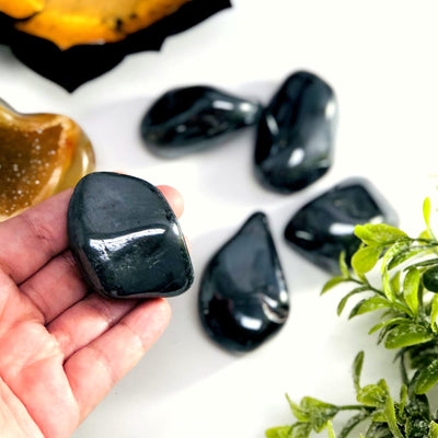 hand holding up hematite tumbled stone with other blurred on white background