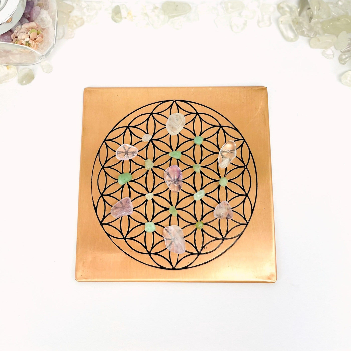copper square flat plate with a flower of life grid in black on it held in a woman's hand displayed with assorted crystals on the grid