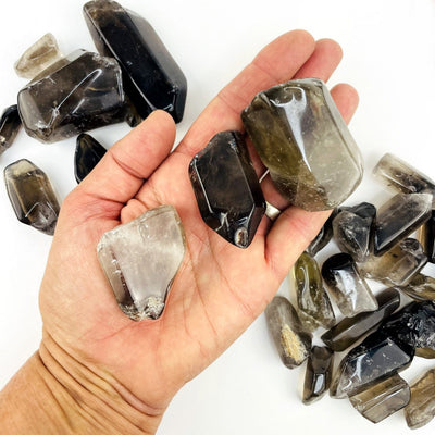 Polished Smoky Quartz Tumbled Stones and Points on a table and in a hand for size reference