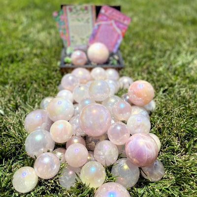 Pile of Rose Quartz Angel Aura Titanium Spheres on grass in front of box filled with more spheres and decorations