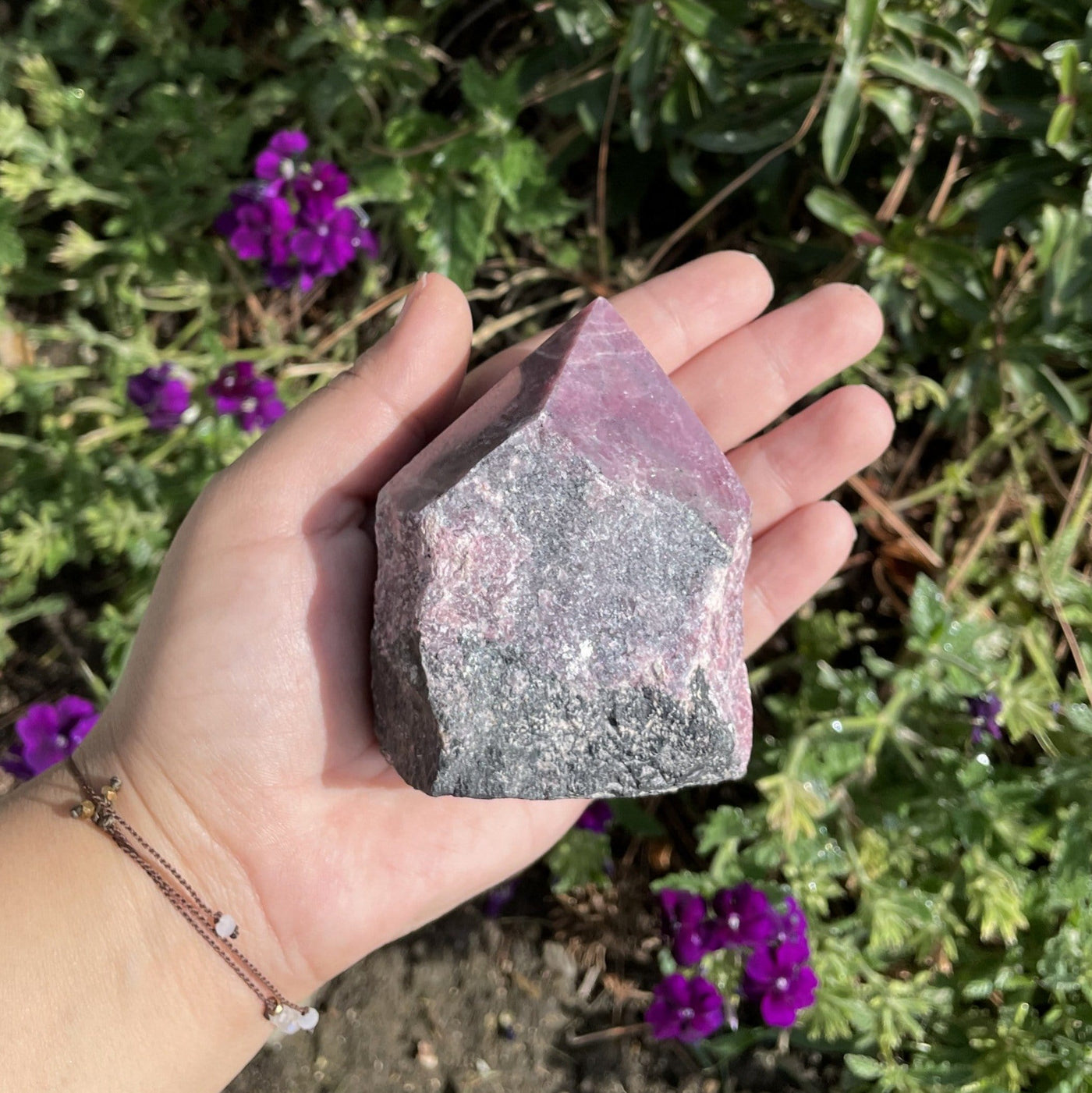 Hand holding up Rhodonite Point in front of plants