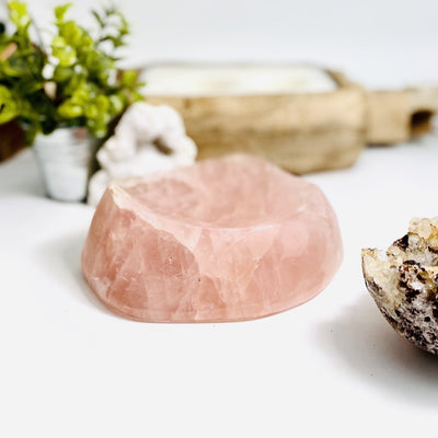 Side view of Rose Quartz Polished Bowl with various decorations in the background