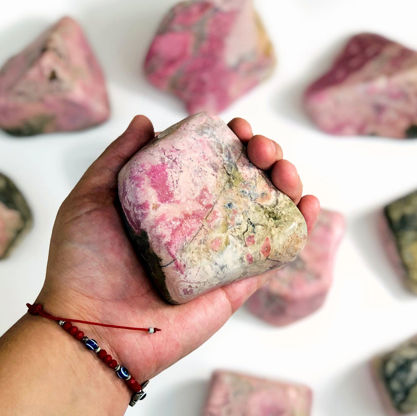 Hand holding up Rhodonite Tumbled Polished Stone with others in the background