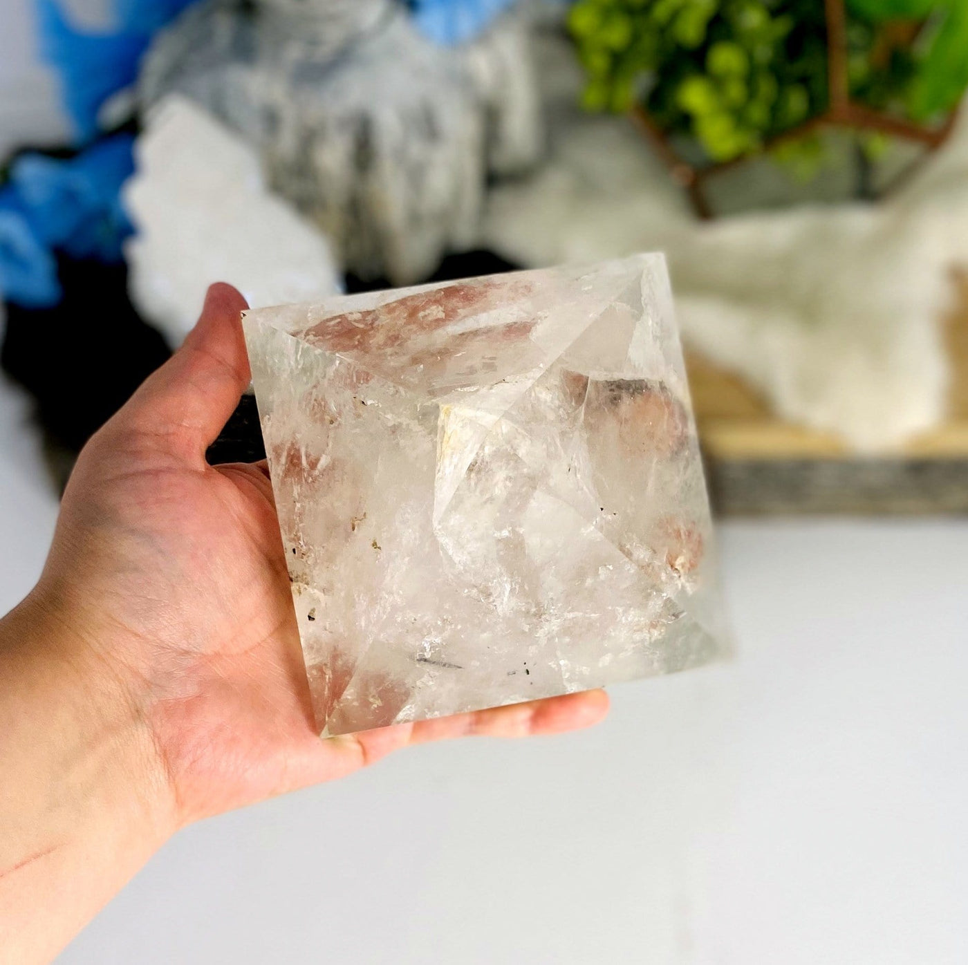 hand holding up Crystal Quartz Pyramid with decorations in the background
