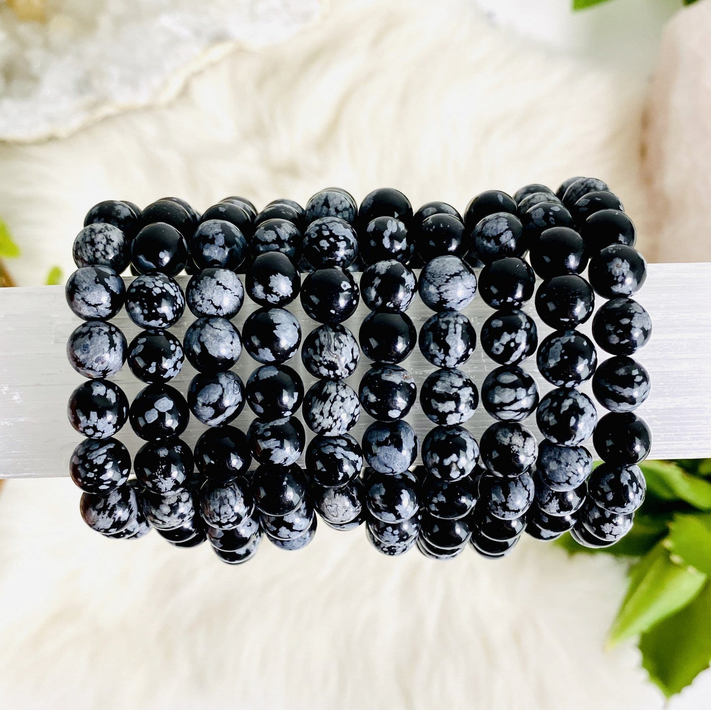 many snowflake obsidian round bead bracelets stacked on display for possible variations