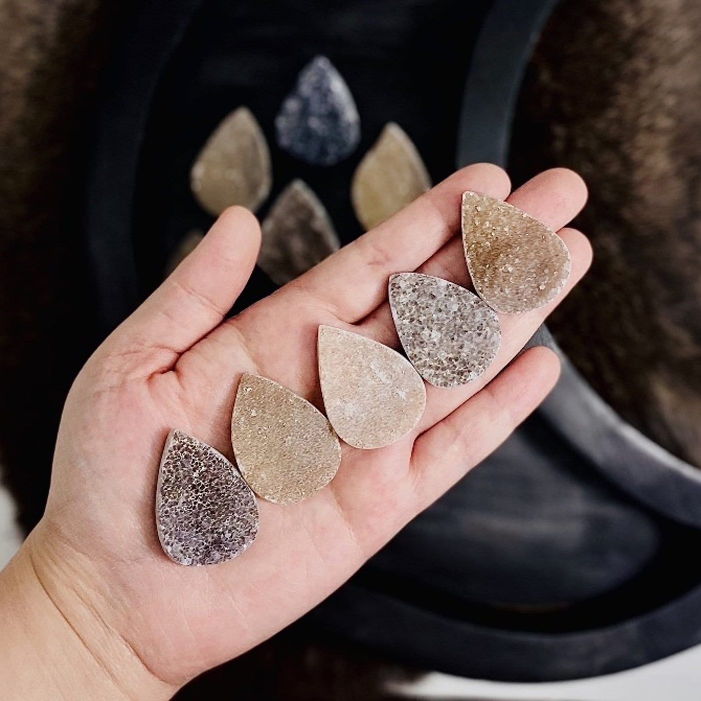 hand holding druzy tear drop cabochons with decorations in the background