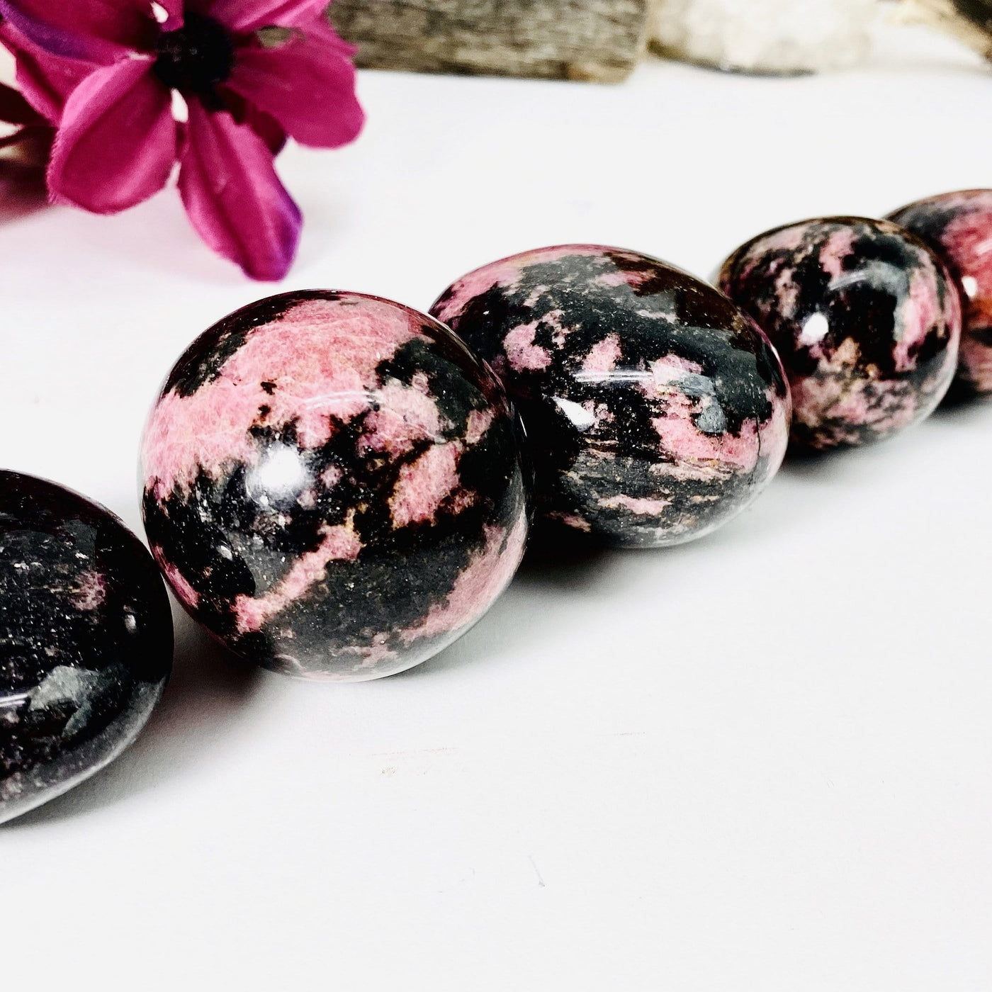 Up close shot of Rhodonite Palm Stones in a line with a red flower in the background
