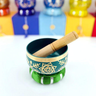 green Brass Tibetan heart Chakra Singing Bowl on top a pillow with a mallet inside