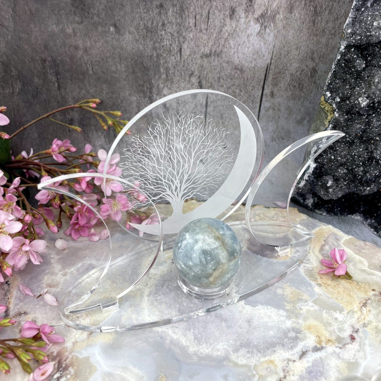 An Acrylic Sphere Holder Crescent Moons - Tree of Life holding a sphere in an alter that consists of flowers and crystals.